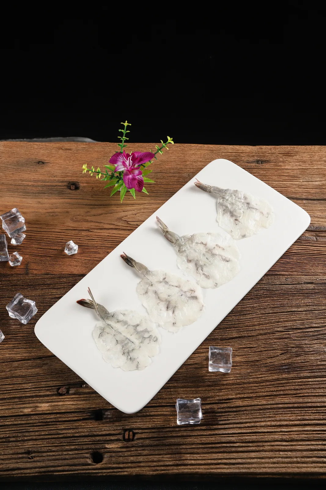 白盘上并排摆着四片生虾片,虾尾完整,盘边散落几块冰